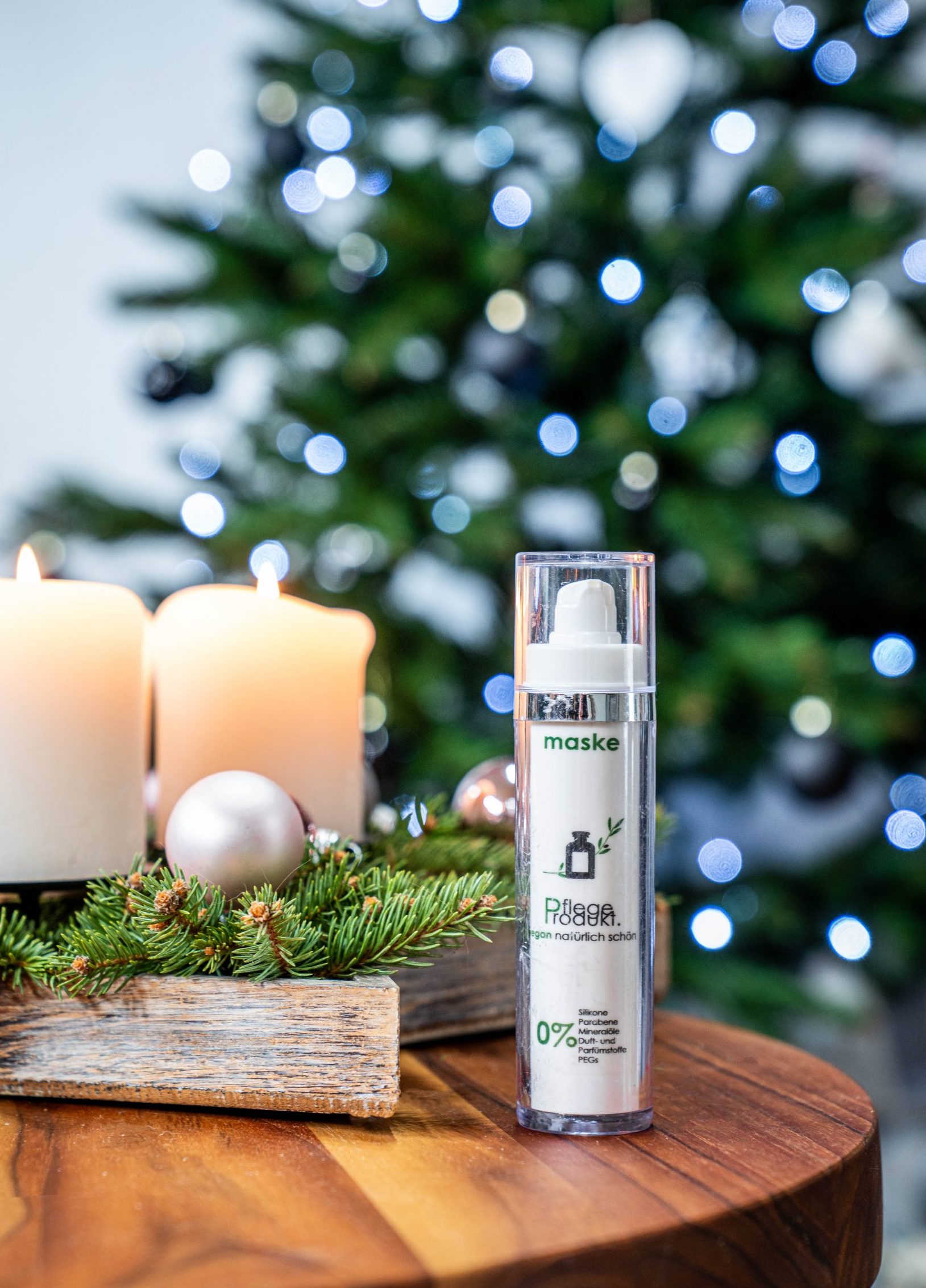 Die Maske von Pflegeprodukt steht auf einem Holzbrett neben einem Weihnachtskranz aus grünen Fichtenzweigen und weißen Kerzen. Im Hintergrund ist ein Tannenbaum zu sehen.